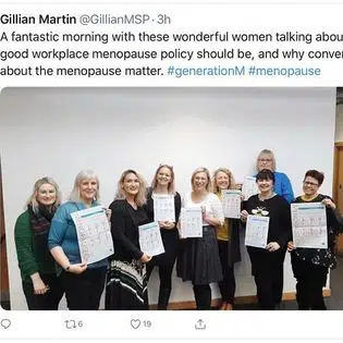 A group of smiling women hold up posters to promote the event.