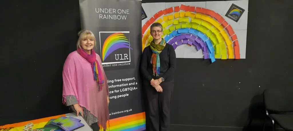 Jools Bell and Maggie Chapman stand in front of a banner at the launch of new LGBTQIA+ charity Under One Rainbow